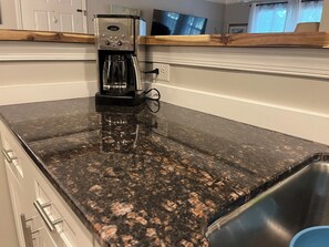 Cocina con cafetera sobre encimera de granito, pileta de acero inoxidable y una barra de madera.