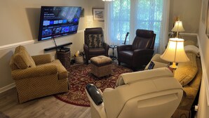 Ein Wohnzimmer mit Flachbildfernseher, zwei Ledersesseln, einem kleinen Tisch, einer Lampe und einer Gitarre.