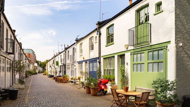 Calle adoquinada flanqueada por edificios tradicionales, con mesas al aire libre y macetas con plantas.