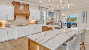 Une cuisine moderne avec des meubles blancs, un îlot en marbre et des luminaires suspendus.