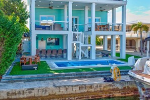 A two-story house with a pool, outdoor seating, and a boat docked nearby. - Summerland Serenity – Elevated Waterfront Luxury with Private Elevator & Pool (Summerland Key)