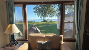 Ein Wohnzimmer mit einem beige gefärbten Sofa, einer Lampe und Blick auf eine Wiese und einen Baum durch große Fenster.