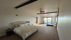 Ein geräumiges Schlafzimmer mit einem großen Bett, einem Deckenventilator und Blick ins Freie durch eine Schiebetür.