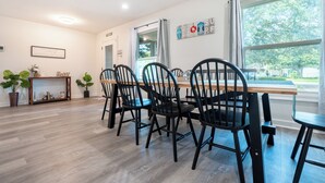 A dining area with a wooden table and black chairs, a ceiling fan, and a window with a view of trees. - Spacious 4-bedroom house in Fort Walton Beach with lots of parking. (Fort Walton Beach)