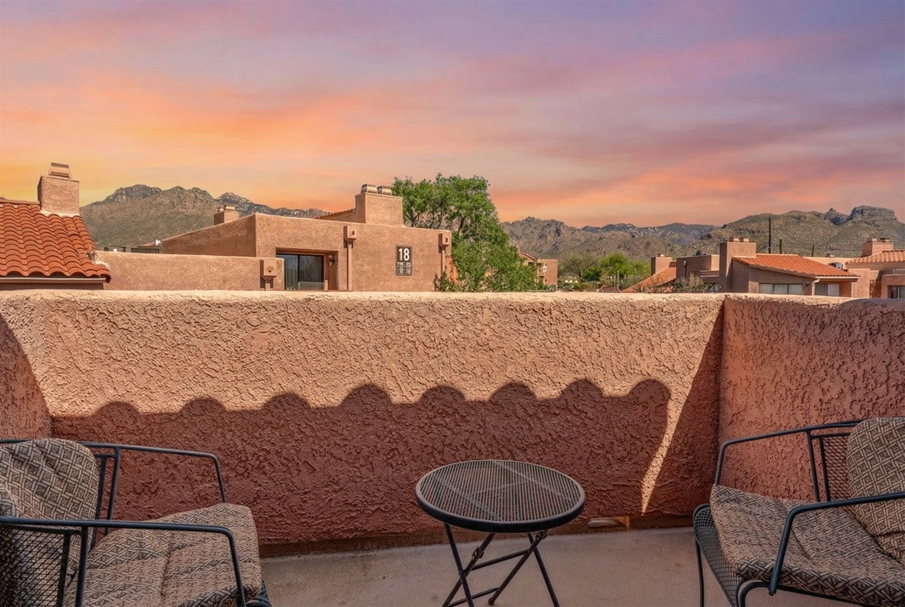 A rooftop terrace with a view of mountains, a wall with a number sign, and two chairs.