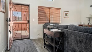 Ein Wohnzimmer mit einer Couch, einem Beistelltisch, einer Tür mit Metallgitter und einem Fenster mit Jalousien.