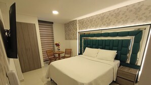 A hotel room with a large bed, a bedside table, a chair, a small table with a vase of flowers, and a mirror above the bed. - New Hotel Vip (Bogotá)