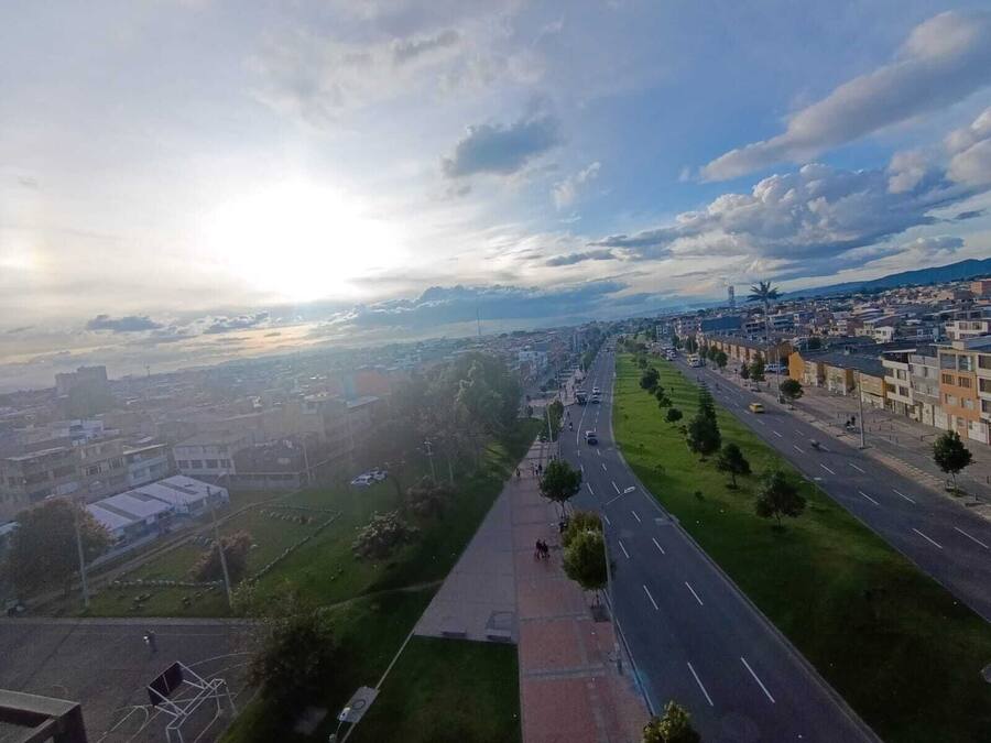 Une large rue bordée de bâtiments des deux côtés, un trottoir pour les piétons et un ciel dégagé.