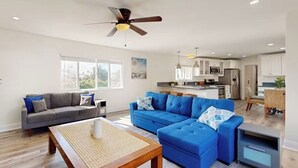A spacious living area with a grey sofa, a blue sectional sofa, a wooden coffee table, and a ceiling fan.