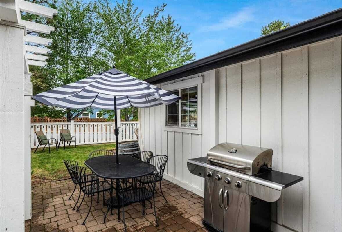 Un patio con una parrilla, una mesa con sillas y una sombrilla.