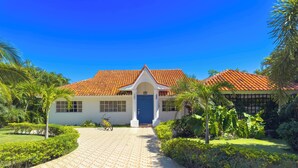 A house with a tiled roof, a paved driveway, and a well-maintained garden with palm trees and shrubs.