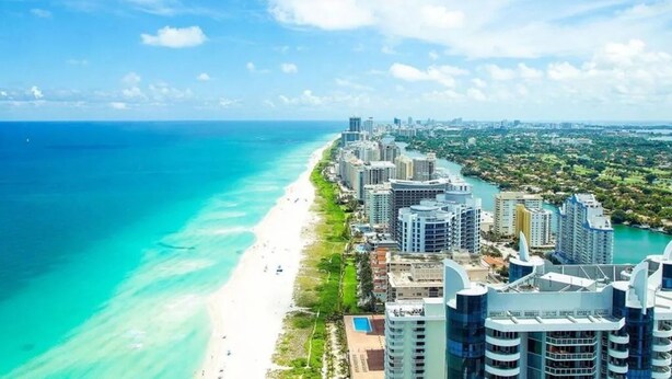 A coastal cityscape with a beach, high-rise buildings, and a clear sky.