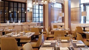 A restaurant with multiple tables set for dining, featuring pendant lighting and large windows.
