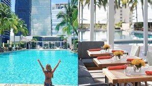 A pool area with a view of One Broadway hotel, outdoor seating with tables and umbrellas, and a person by the pool.