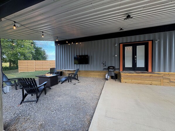 An outdoor patio area with a fire pit, seating, a grill, and a TV mounted on the wall.