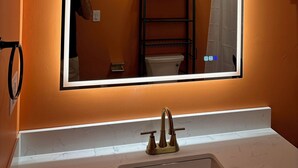 Ein Badezimmer mit einem großen Spiegel, einem Waschbecken mit goldfarbenem Wasserhahn und drei Wandbildern, die verschiedene Szenen zeigen.