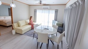 A modern hotel room with a bed, a sofa, a dining table with chairs, and a large window with curtains. - Exclusive view of the star-filled sky on the rooftop terrace. Walking distance from Imgarma Marine Garden (1.1km). Privileges: Free Miyako soba noodles, BBQ set rental, and star photography can be arranged. Unattended check-in support. (Miyaknjima)
