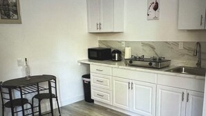 A compact kitchen with white cabinets, a microwave, a coffee maker, and a sink. There is a small dining table with chairs. - The palm trees (Las Vegas)