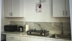 A kitchen with white cabinets, a microwave, a gas stove, a sink, and a wall-mounted wine glass decoration. - The palm trees (Las Vegas)