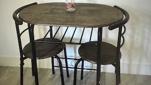 A round metal table with three chairs, a clear vase with flowers, and a white wall in the background. - The palm trees (Las Vegas)
