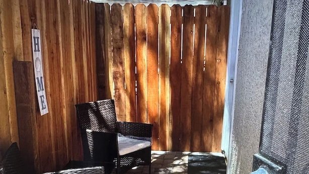 A covered patio area with wicker furniture and a wooden fence. - The palm trees (Las Vegas)