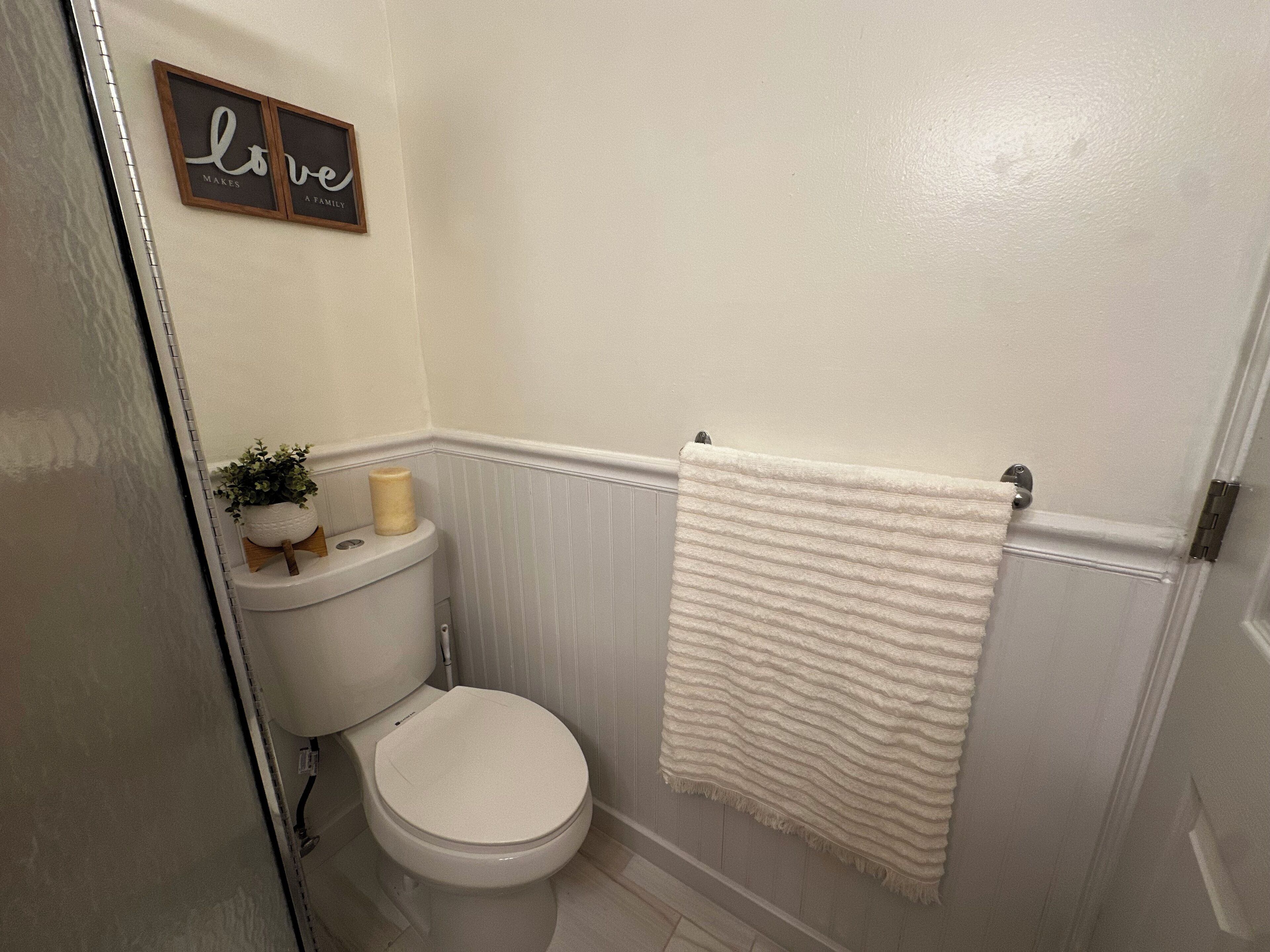 A bathroom with a toilet, a towel hanging on the wall, and a sign that says "Love Makes a Family".