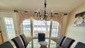 A dining room with a glass table surrounded by chairs, a chandelier, and large windows with a view of the outdoors.