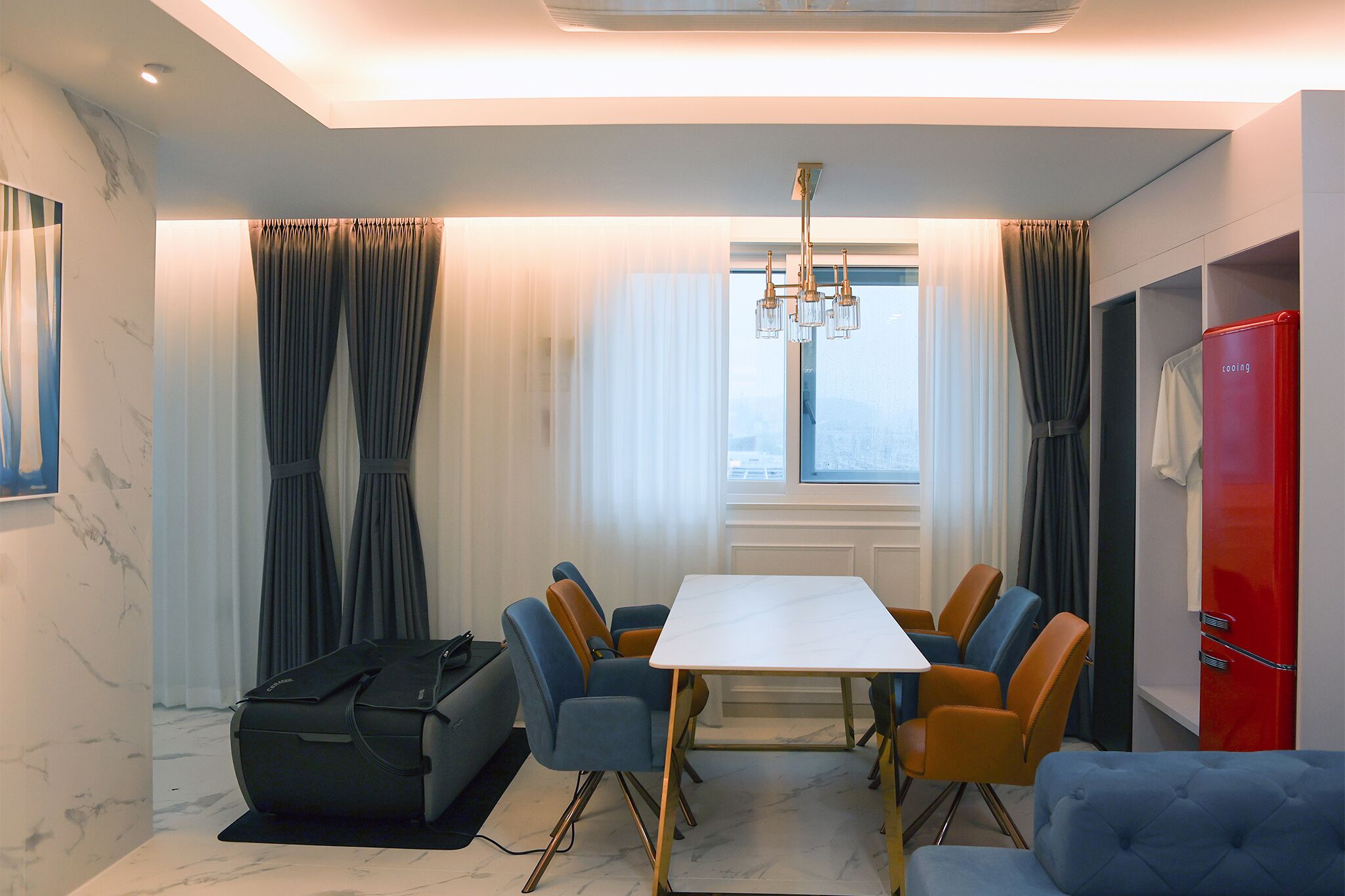 A modern hotel room with a dining area featuring a white table and blue and orange chairs.