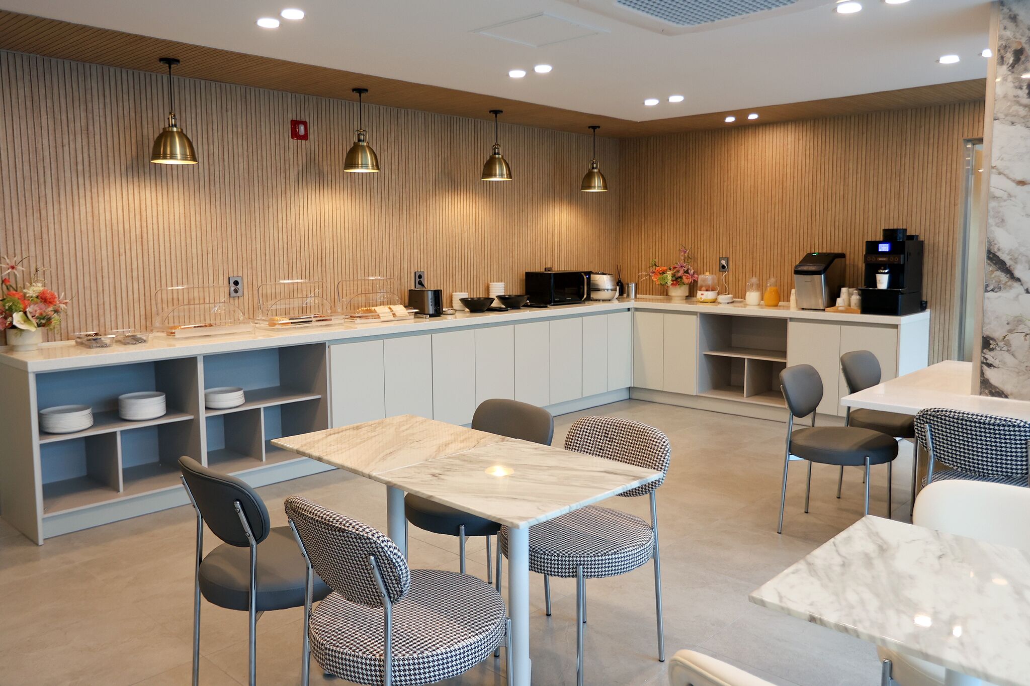 A modern kitchen with a marble countertop, pendant lighting, and a coffee machine.