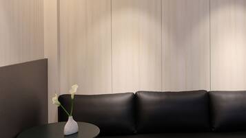Un interior modern amb un sofà de pell negra, una taula rodona petita i un vas de flors blanc.