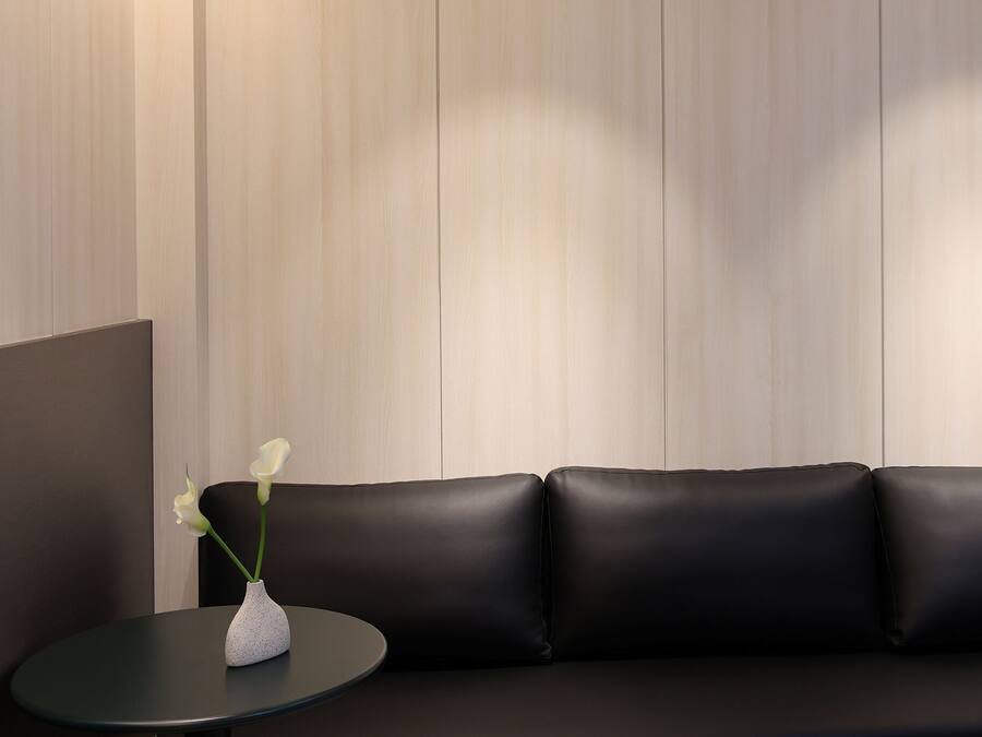 Un interior modern amb un sofà de pell negra, una taula rodona petita i un vas de flors blanc.