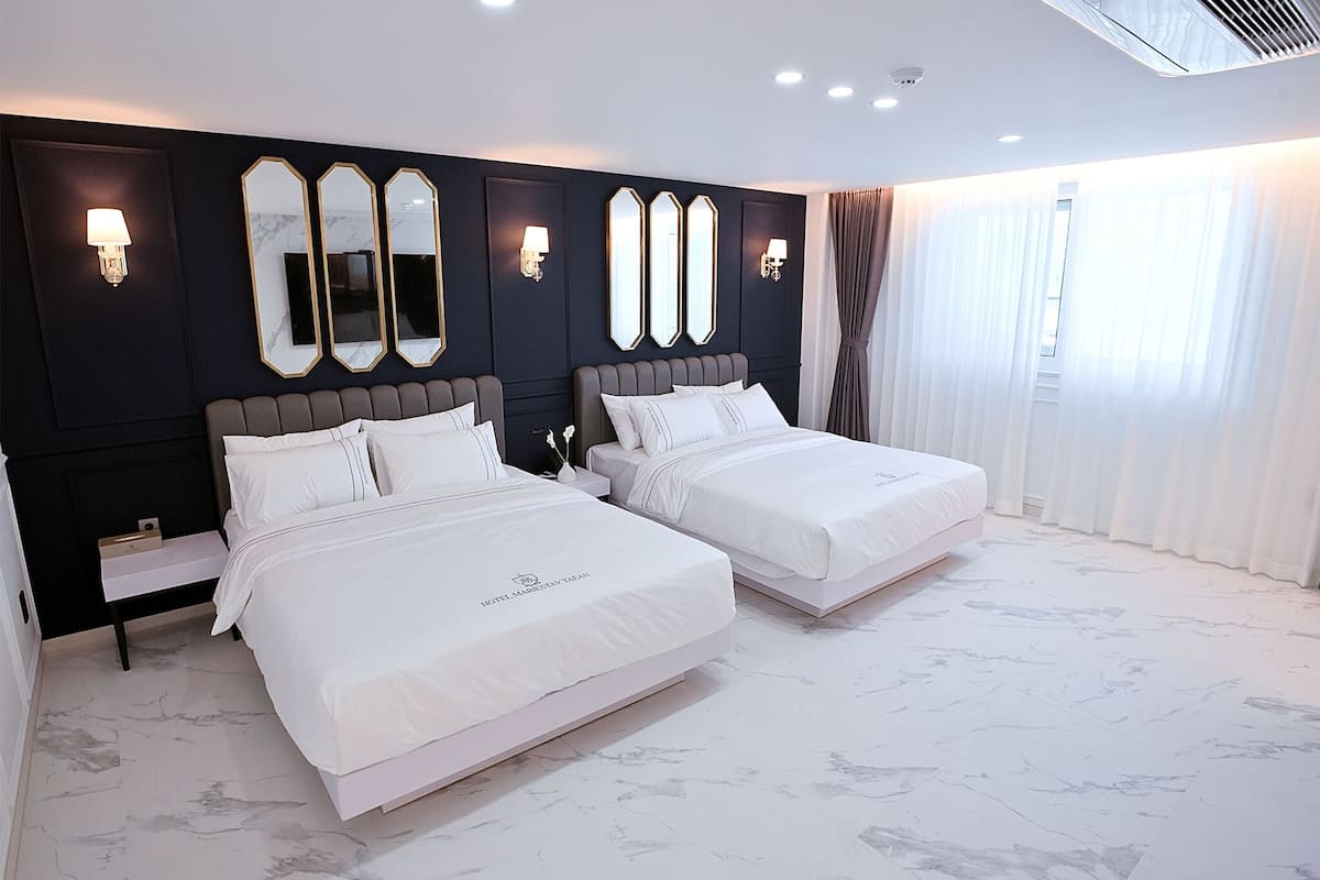 A hotel room with two beds, marble flooring, and a dark wall with decorative mirrors and wall sconces.