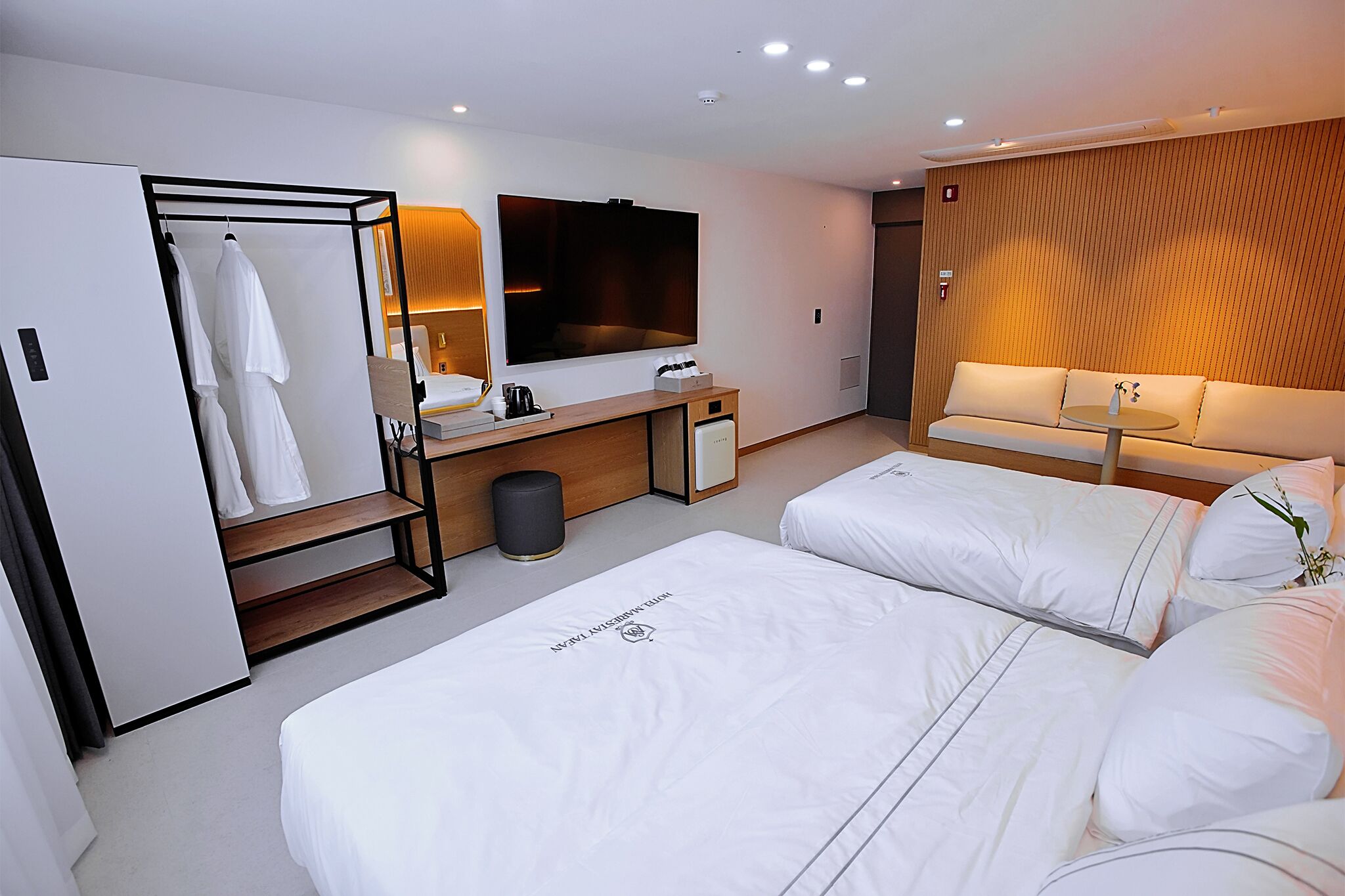 A modern hotel room with a large bed, a sofa, a TV, a desk, and a wardrobe.