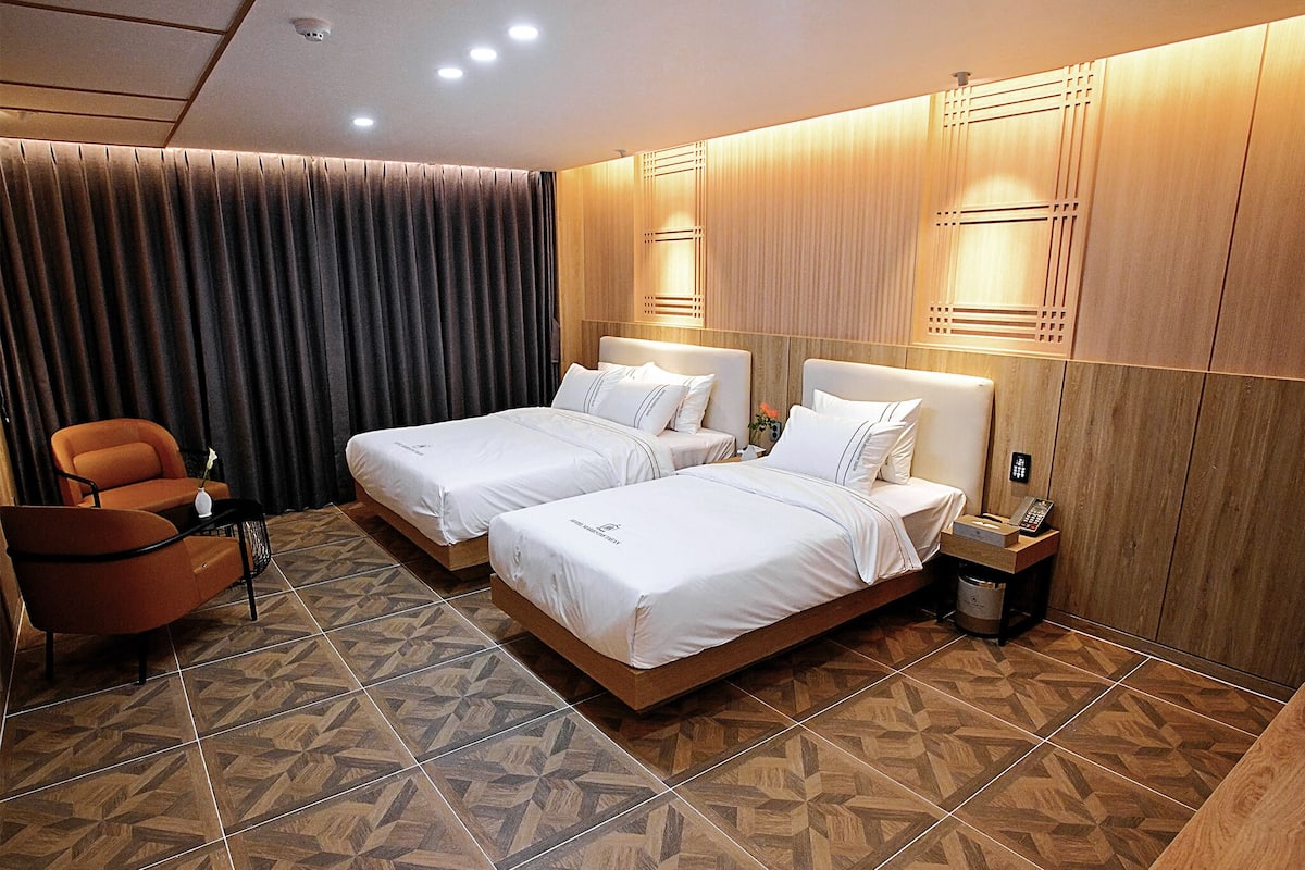 A hotel room with two beds, a sofa, a waste bin, and a phone on a nightstand.