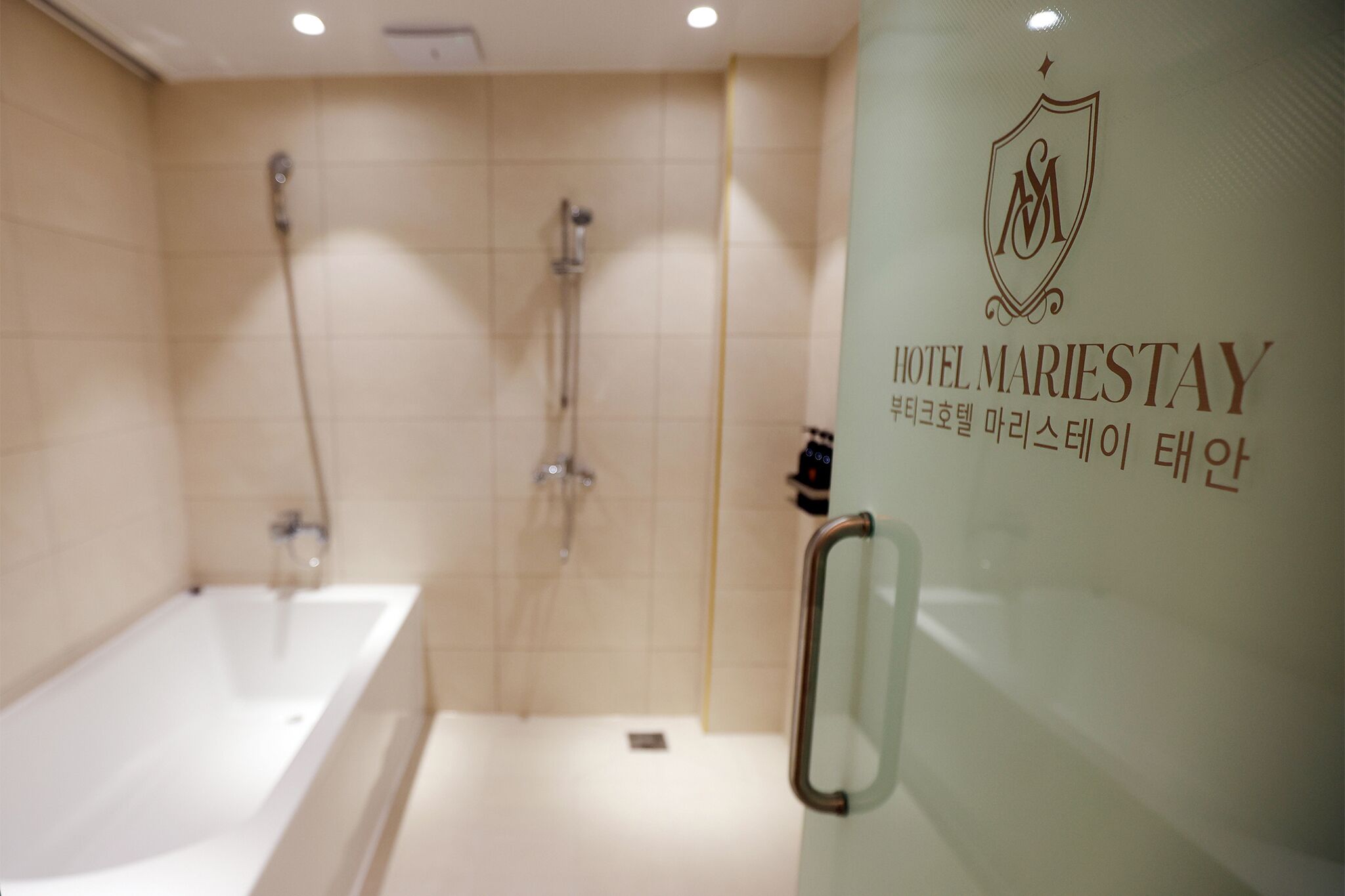 Baño de hotel con bañera, ducha y separador de vidrio con un logotipo y texto.
