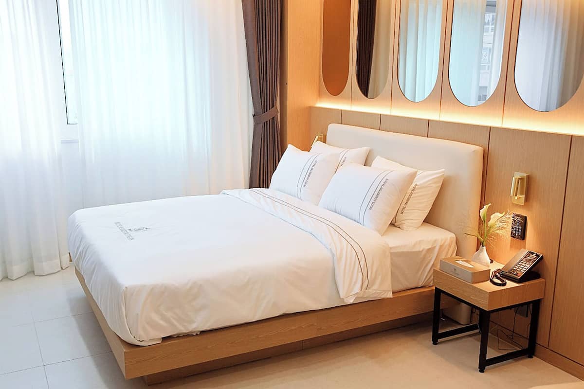 A modern hotel room with a large bed, a bedside table with a lamp, and a mirror above the bed.