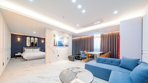 A modern hotel room with a large bed, a seating area with a table and chairs, a blue sofa, and a marble coffee table. - HOTEL MARIESTAY TAEN (Taean)