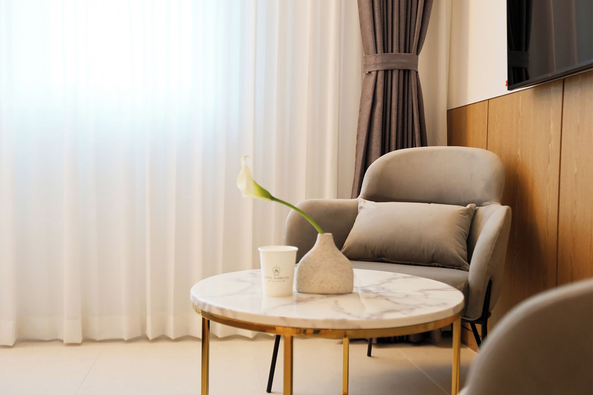 A modern living room with a round marble table, a beige armchair, a white vase with a plant, and a white cup.