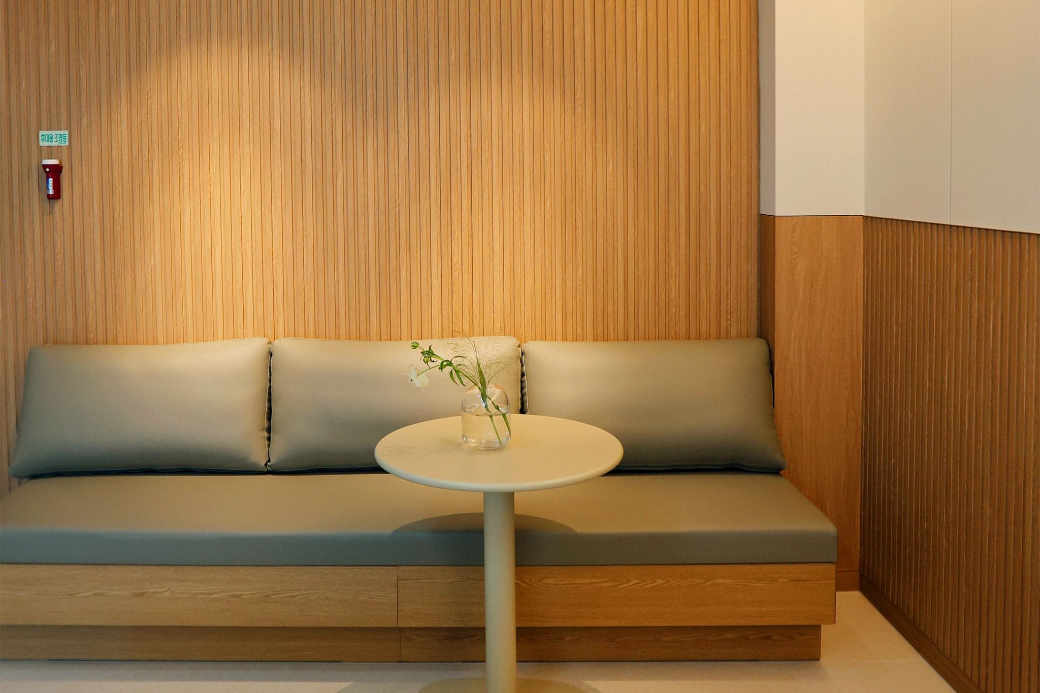 A modern room with a wooden panel wall, a beige sofa, and a small round table with a vase of flowers.