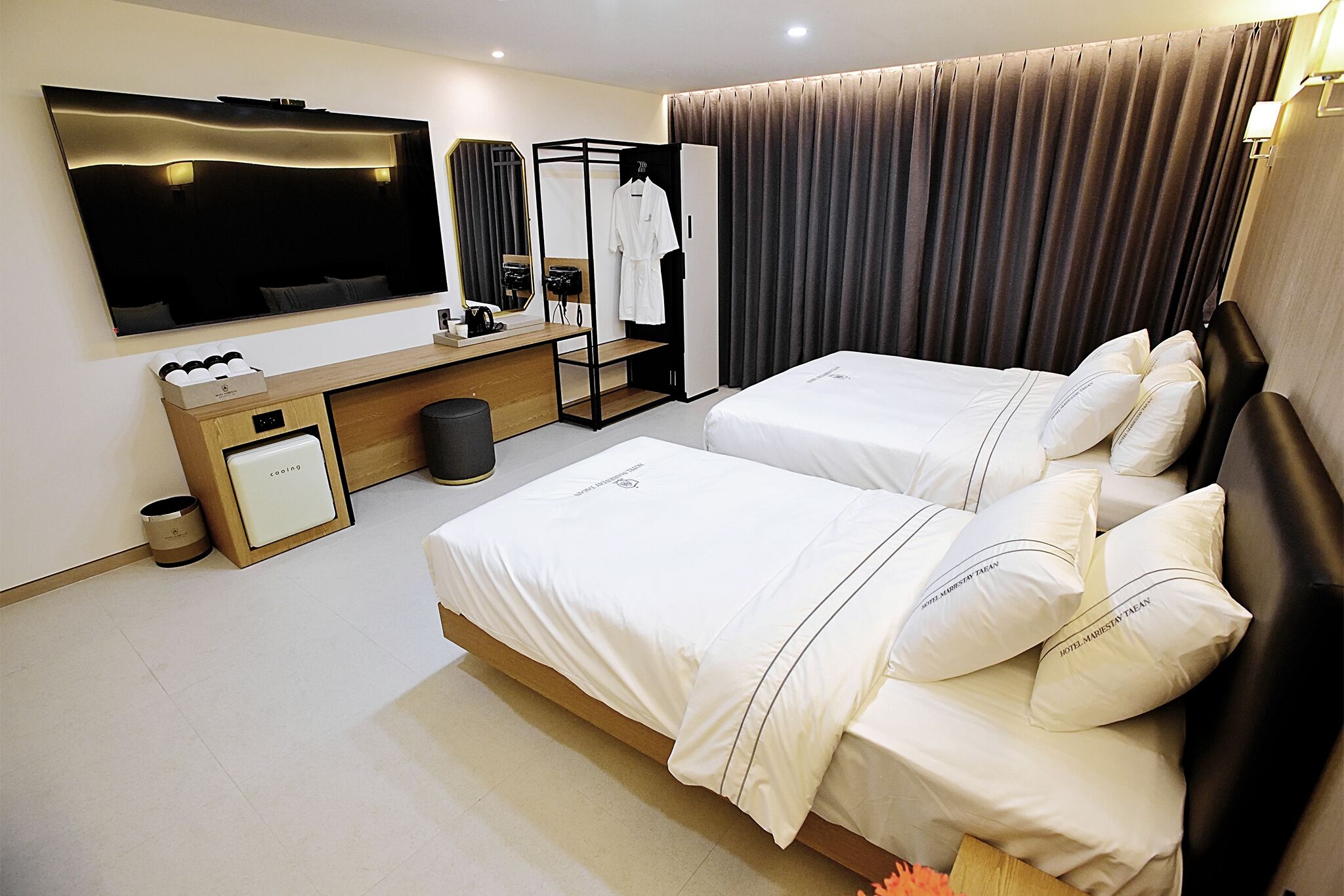 A hotel room with two beds, a TV, a desk with a computer, and a wardrobe.