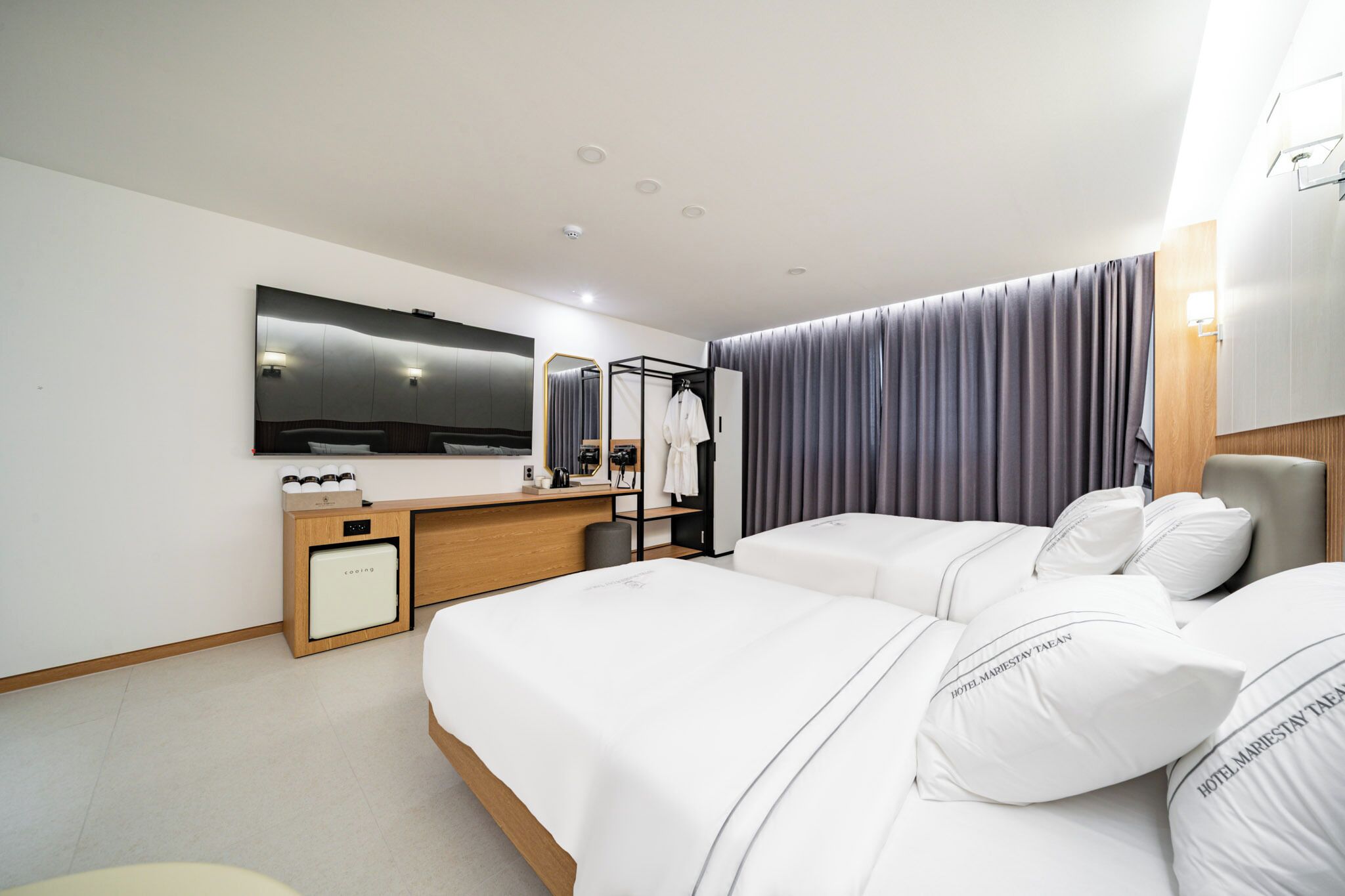 A modern hotel room with two beds, a desk, a television, and a mirror.