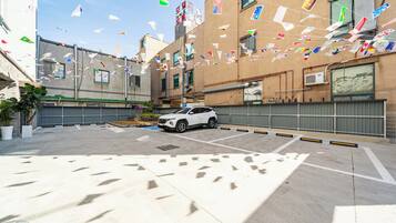 A parking area with a white SUV, surrounded by buildings with multiple flags.