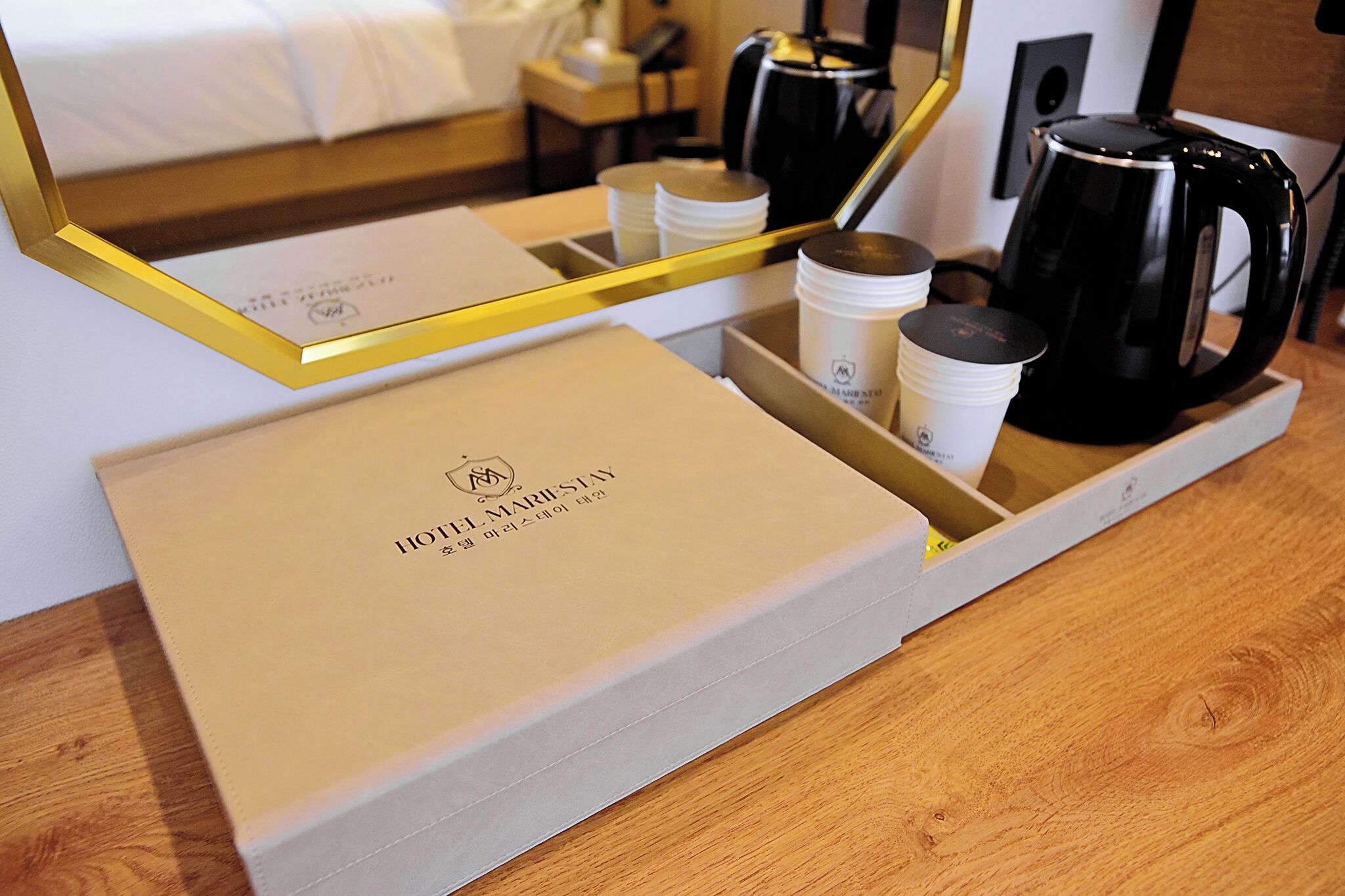 A hotel room with a bed, a bedside table, a coffee maker, and a tray with cups and a box.