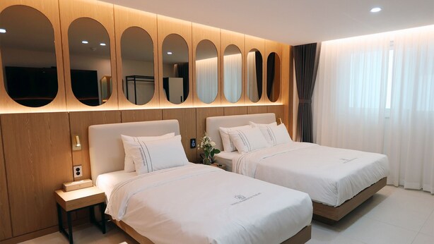 A hotel room with two beds, a wooden headboard, a nightstand, and a mirror wall. - HOTEL MARIESTAY TAEN (Taean)