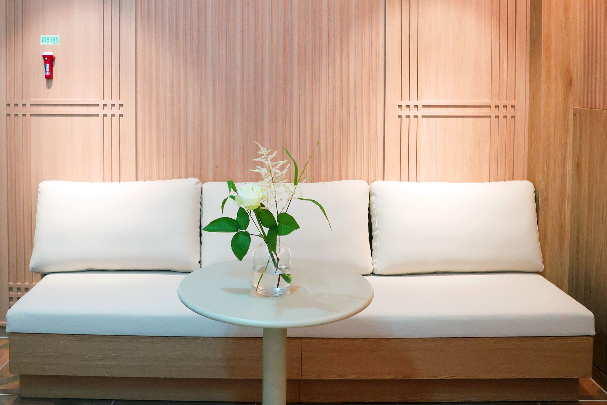 Quarto de hotel moderno com um sofá branco, uma pequena mesa redonda e um vaso com flores.