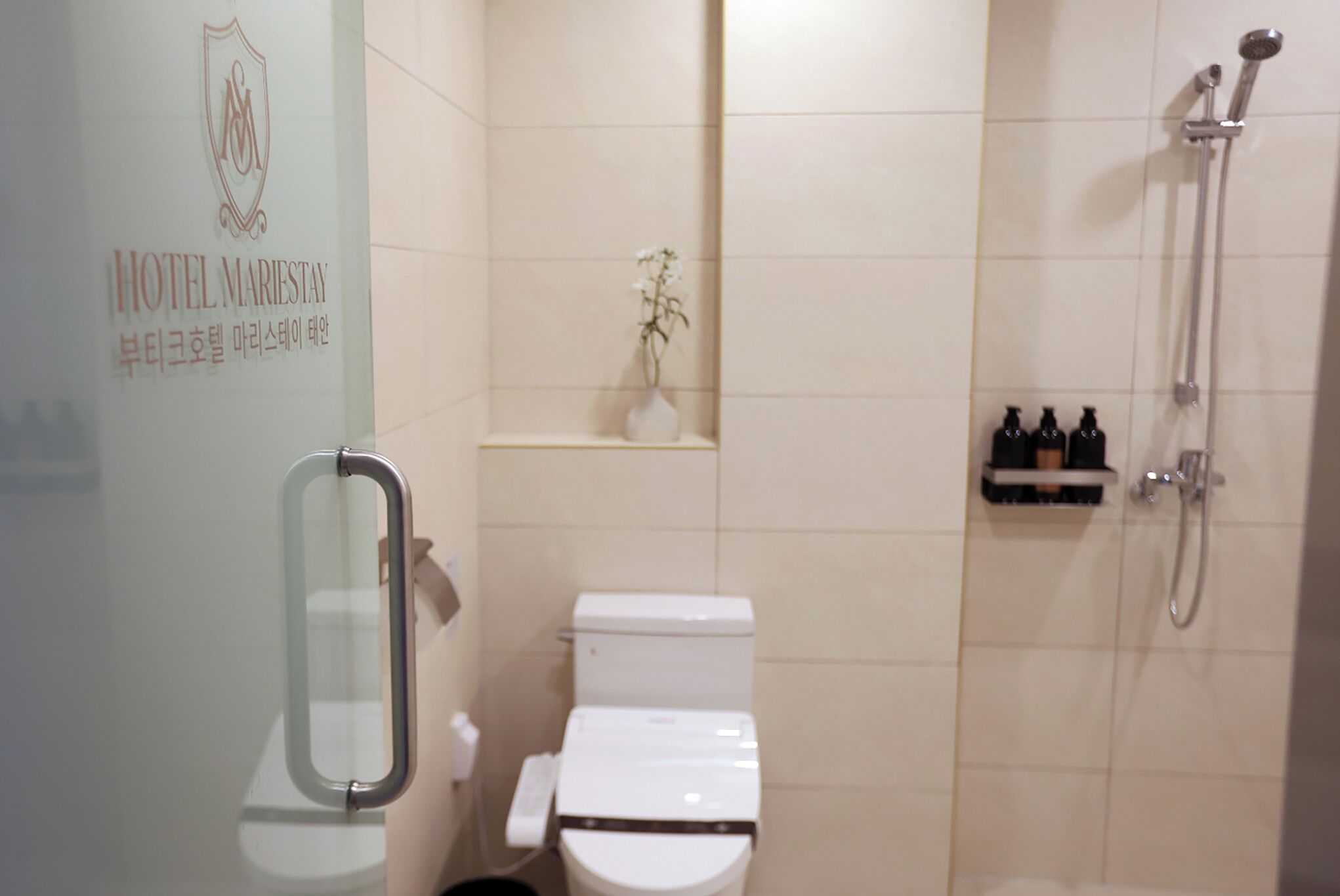 A bathroom with a toilet, a shower, and a small shelf with toiletries.