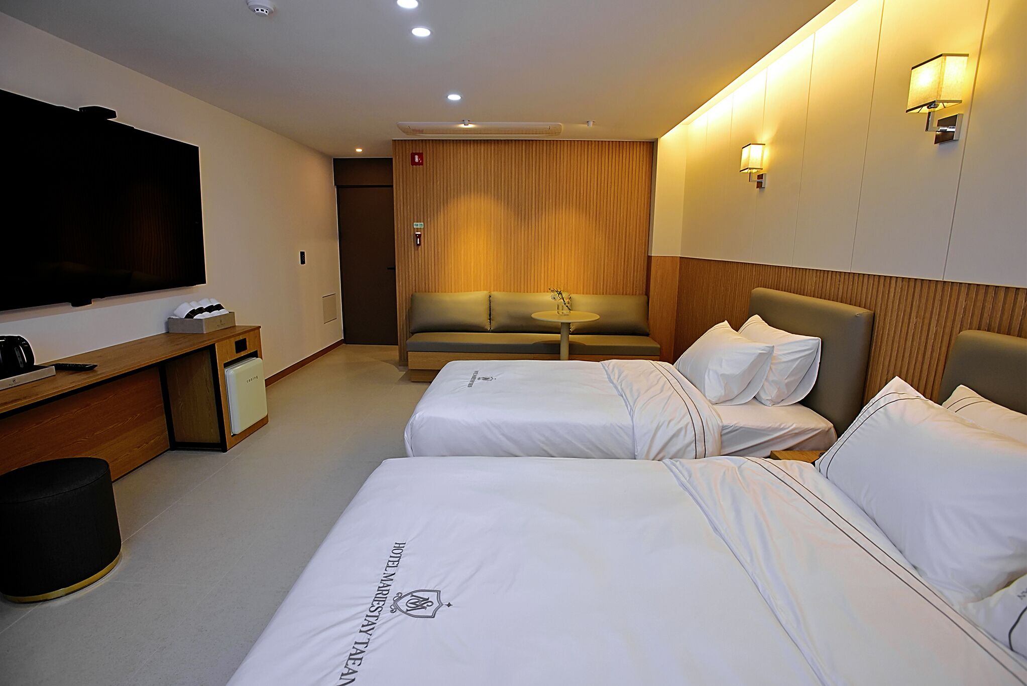 Quarto de hotel com duas camas, um sofá, uma TV, uma escrivaninha e uma pequena mesa.