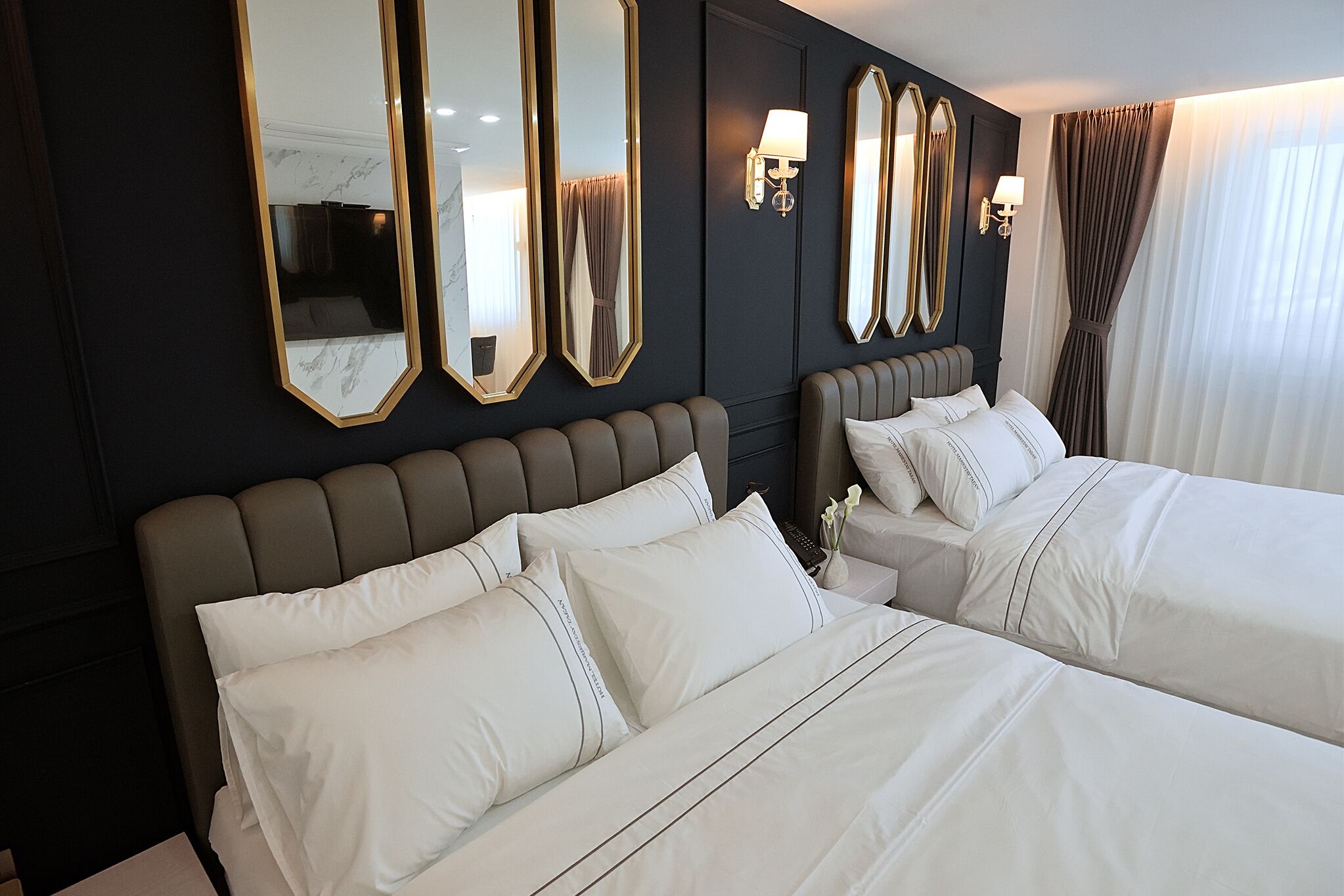 Quarto de hotel com duas camas, paredes escuras e grandes espelhos.