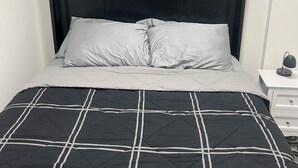 A bed with a black and white checkered bedspread, a dark headboard, and three wall-mounted paintings above. - New basement suite in Saskatoon's newest neighborhood. Welcome to the Casa! (Saskatoon)