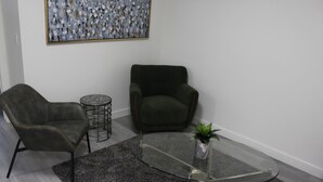 A modern living room with a glass coffee table, two armchairs, a small round table, and a painting on the wall. - New basement suite in Saskatoon's newest neighborhood. Welcome to the Casa! (Saskatoon)